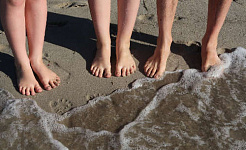 pairs of feet standing on the beach at the edge of the waves coming in to shore